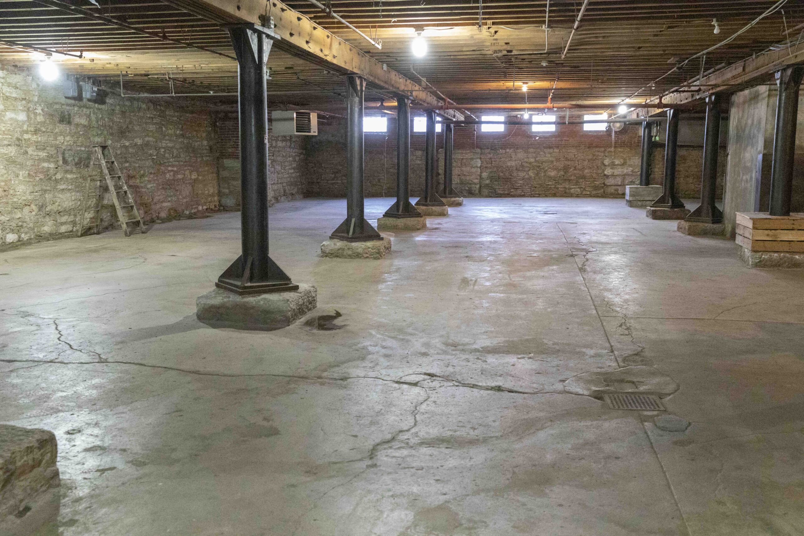 Commercial Real Estate in Kansas City's West Bottoms. Historic basement commercial space in Kansas City's West Bottoms featuring exposed brick walls, concrete flooring, steel support columns, and original industrial architecture.